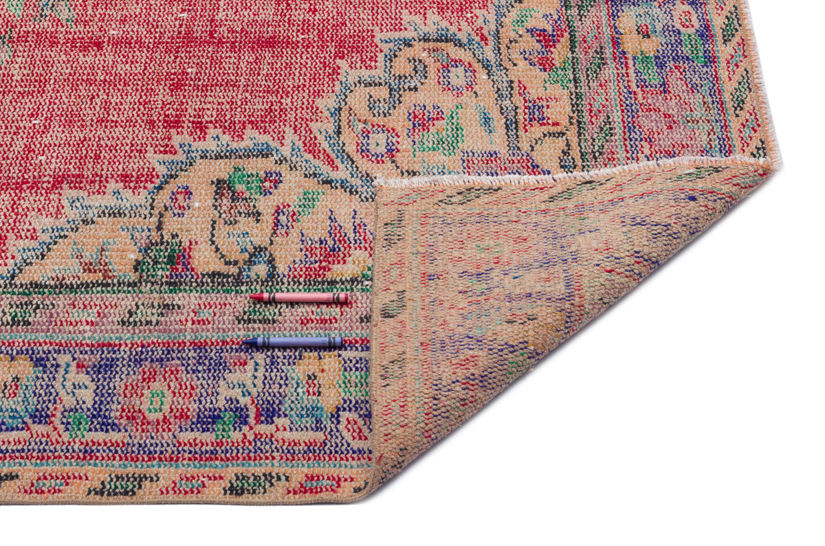 Red and blue distressed vintage-style rug with a floral medallion pattern, shown folded to reveal the tan backing.