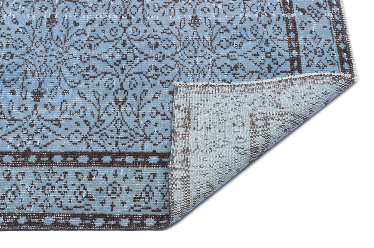 Light blue and brown distressed rug with a traditional floral medallion pattern, shown with a corner folded over.