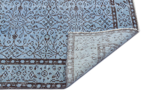 Load image 1 in gallery view. Light blue and brown distressed rug with a traditional floral medallion pattern, shown with a corner folded over.