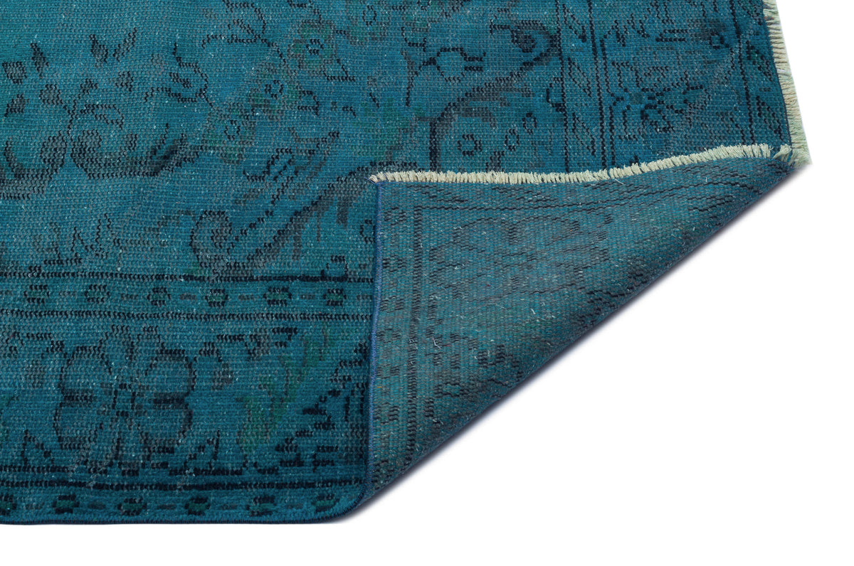 Teal and black distressed traditional rug with a floral medallion pattern, shown with a folded corner on a white background.