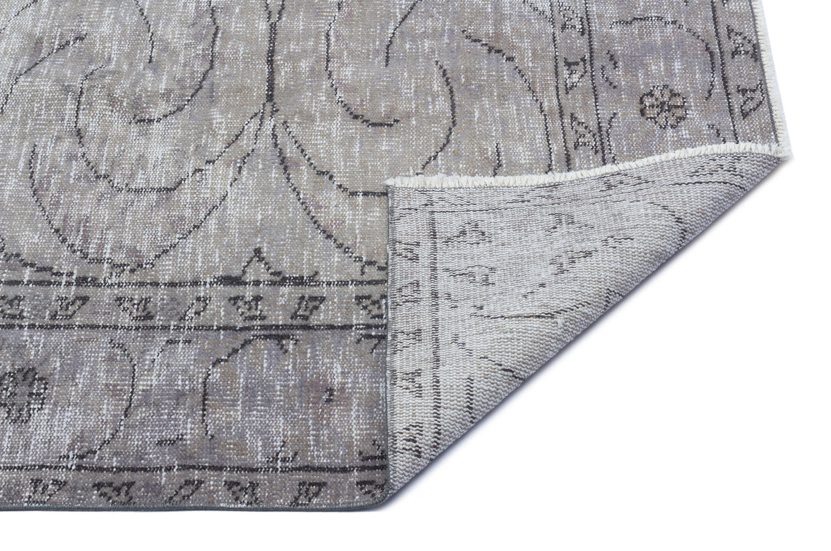 Grey and beige distressed rug with a traditional floral medallion pattern and a folded corner showing the woven backing.