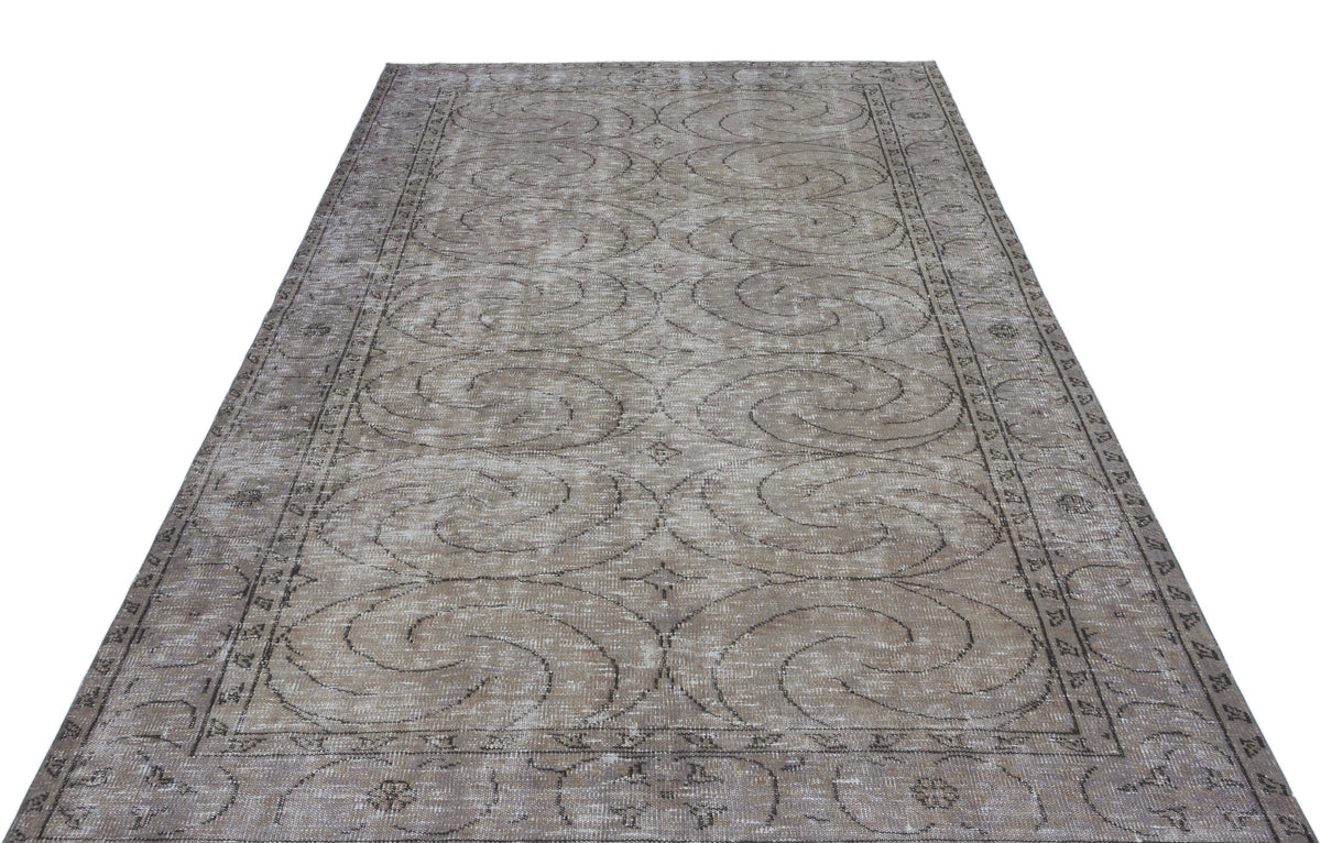 Taupe and grey distressed vintage rug with a repeating spiral medallion pattern and a decorative border.