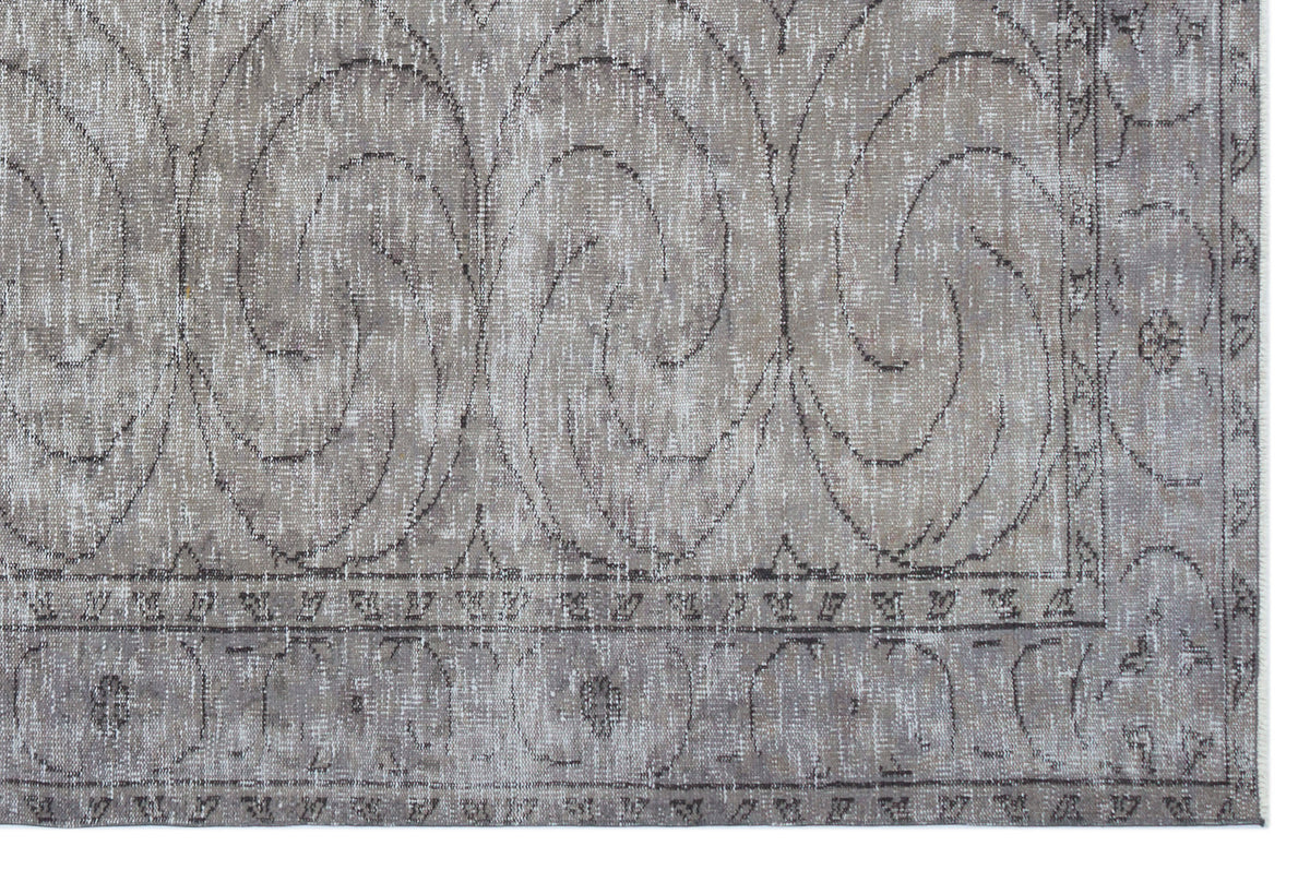 Taupe and grey distressed rug with a large-scale swirling scroll pattern and a decorative geometric border.