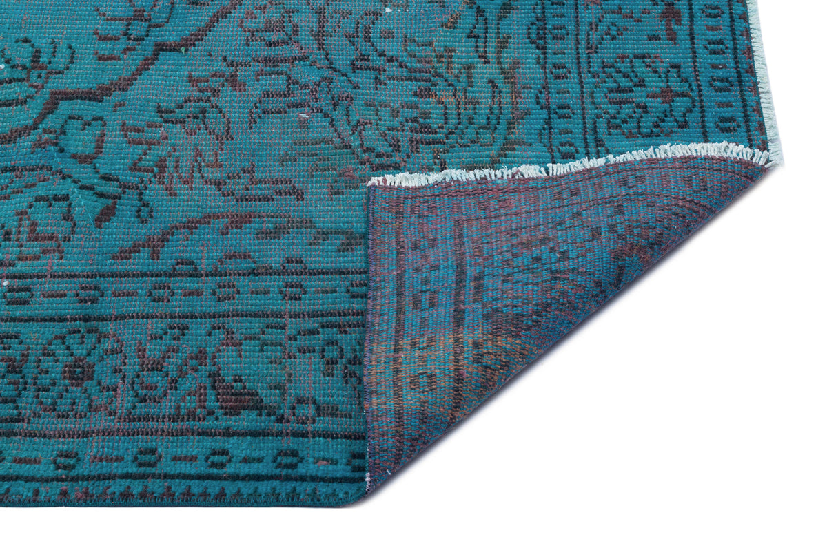 Teal and charcoal traditional rug with a distressed floral medallion pattern, shown with a folded corner on white.