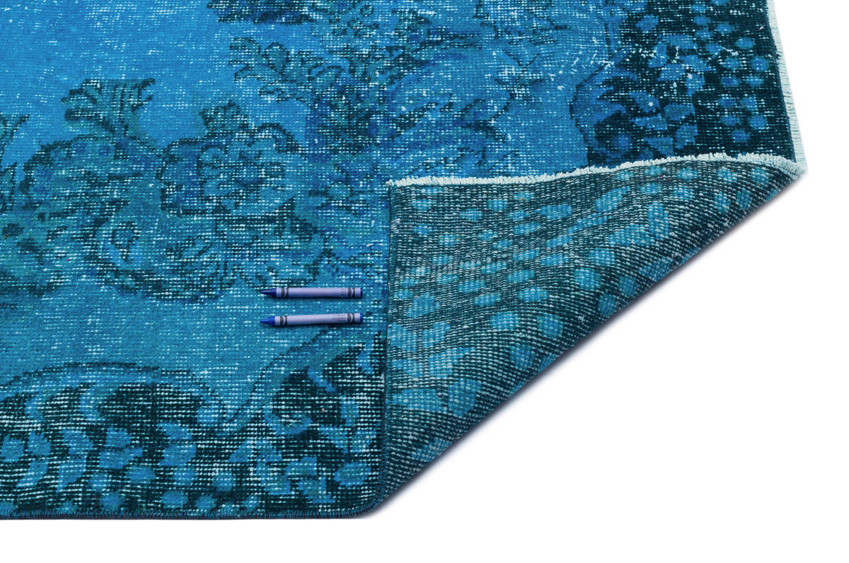 Bright blue distressed rug with a dark floral medallion pattern and a folded corner showing the woven backing.