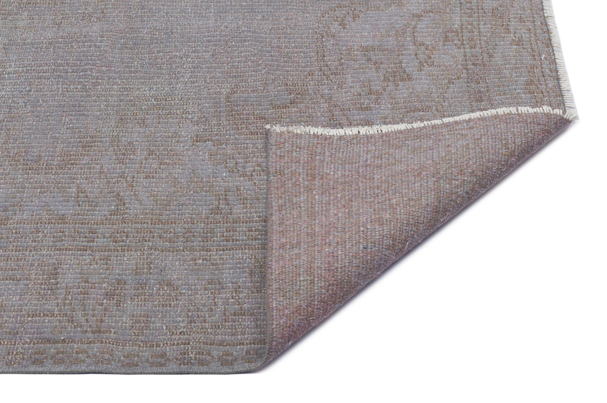 Grey and taupe distressed rug with a faded traditional pattern, shown with a corner folded to reveal the backing.