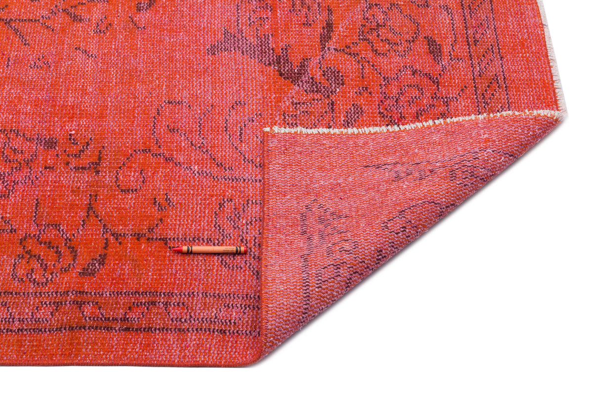 Vibrant orange rug with a dark floral pattern, shown with a corner folded over to reveal the woven backing.