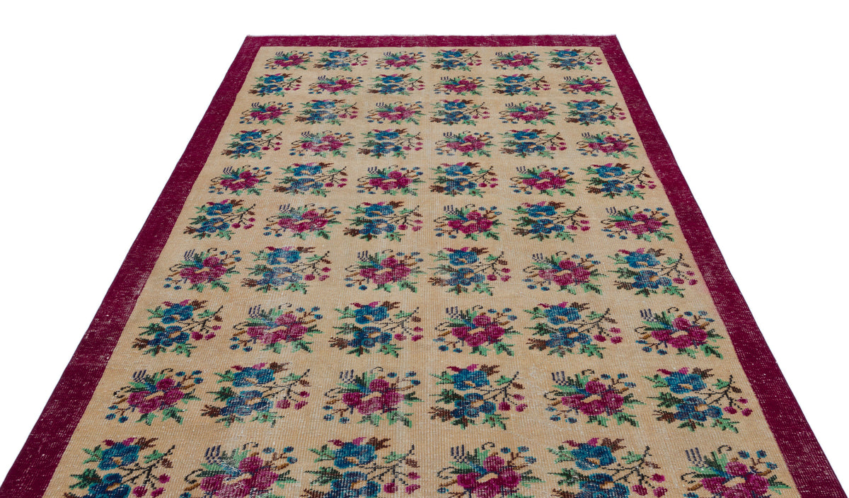 Beige rug with a repeating floral pattern in magenta, blue, and green, framed by a wide magenta border.