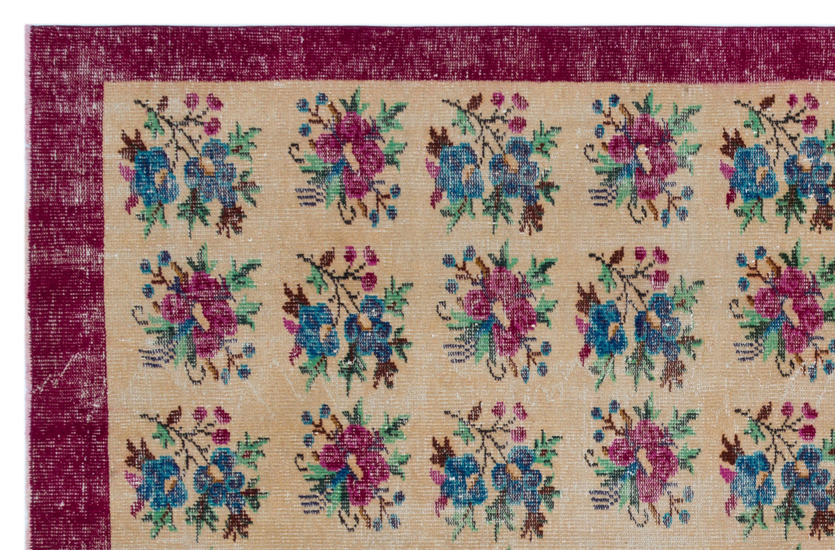 Beige rug with a deep magenta border and a repeating grid of blue and magenta floral bouquets.