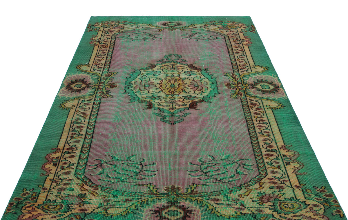 Distressed green and mauve vintage-style rug with a central floral medallion and ornate border on a white background.