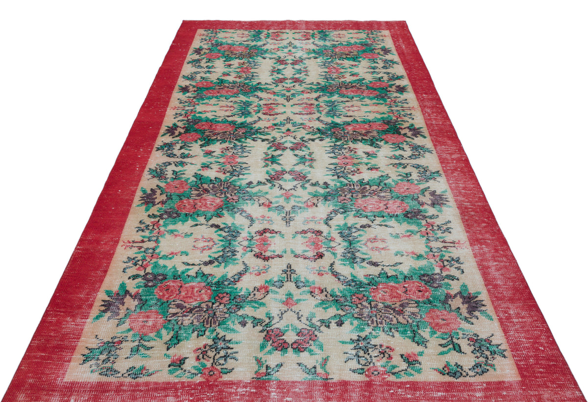 Distressed beige rug with a red border and a repeating floral pattern in shades of red, green, and dark grey.