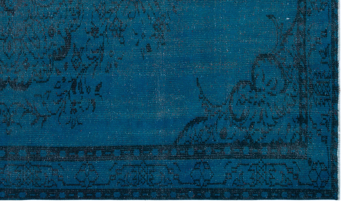 Deep teal rug with a black distressed floral medallion pattern and a geometric border.
