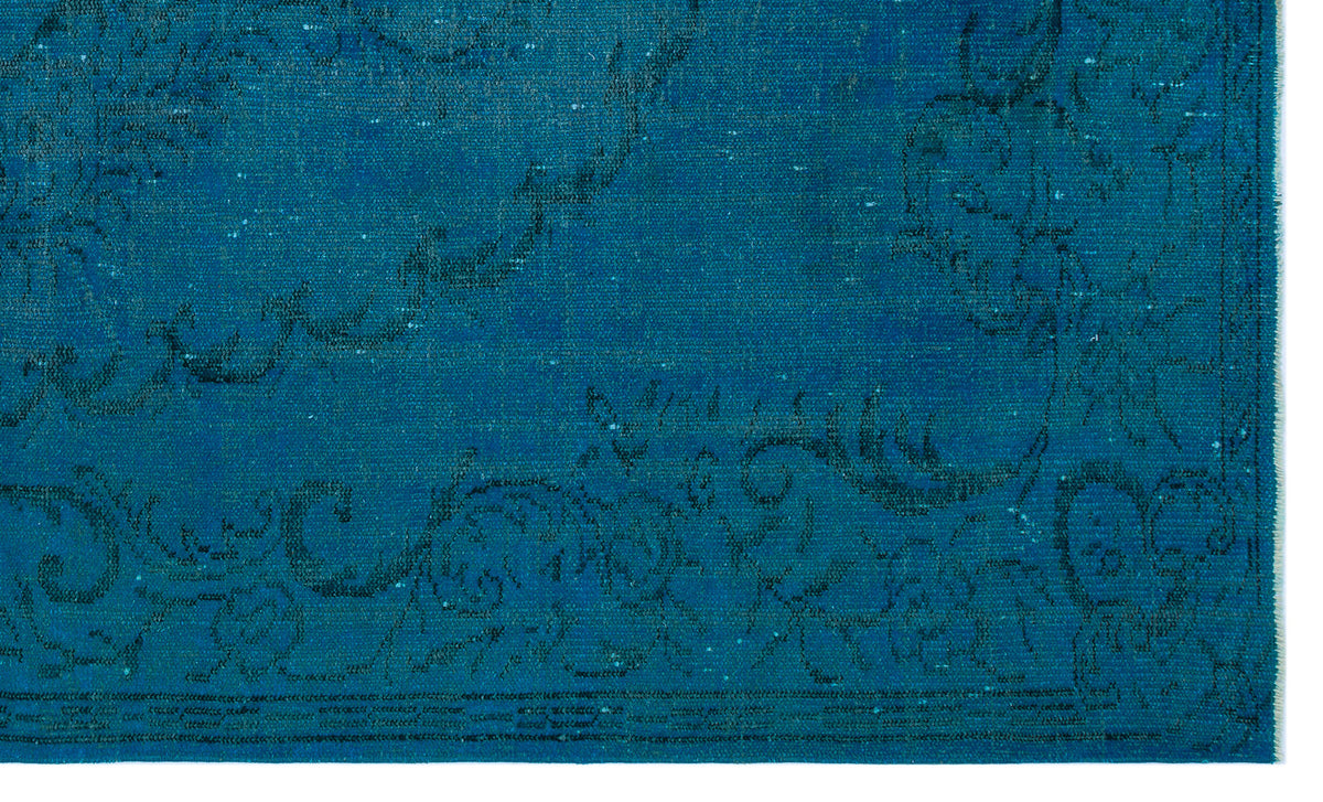 Teal rug with a distressed, dark blue floral medallion pattern and a fringed edge.