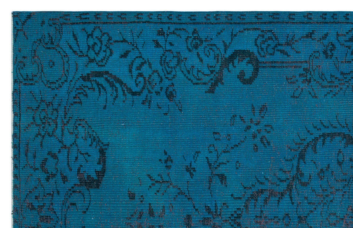 Teal rug with a black distressed floral pattern and a decorative border.
