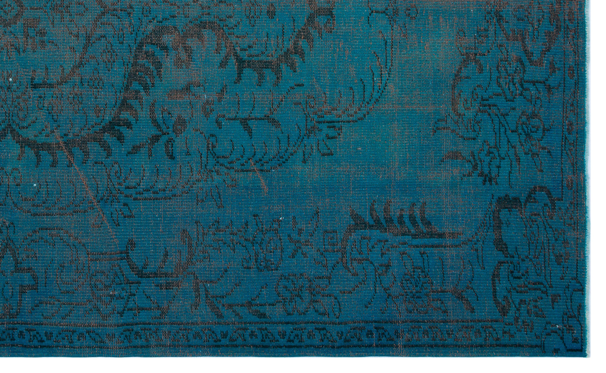 Teal rug with a distressed black floral and vine pattern and a decorative border.