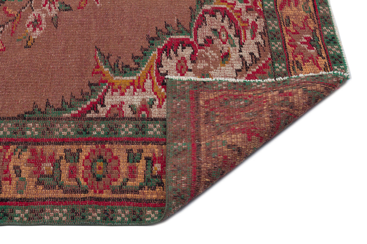 Brown traditional rug with a red, green, and gold floral border, shown with a corner folded over to reveal the backing.