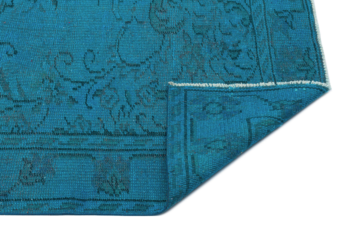 Teal blue rug with a distressed traditional pattern and a folded corner revealing the woven backing.