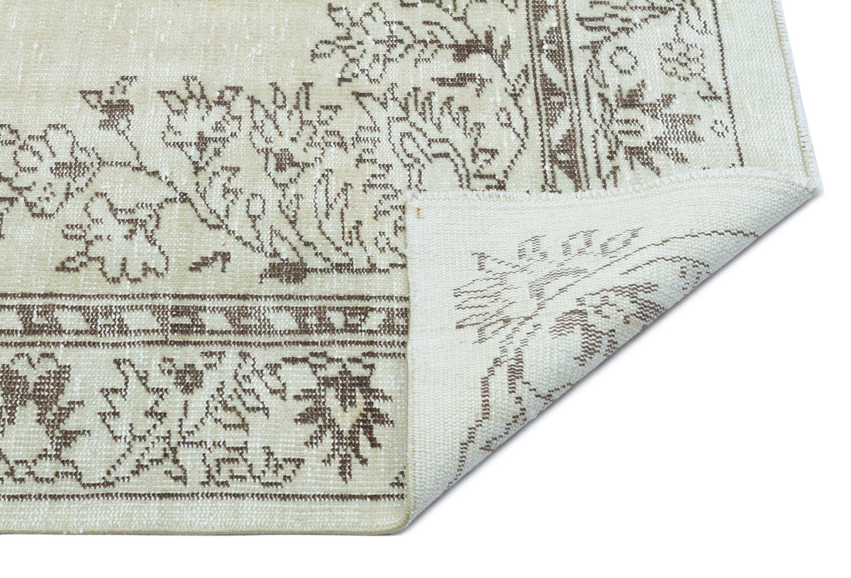 Beige and brown rug with a distressed floral pattern and a folded corner showing the woven backing.