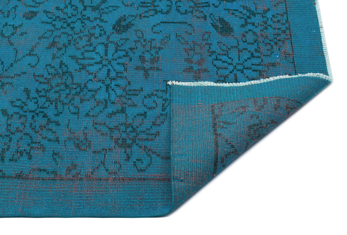 Teal rug with a dark floral pattern and a folded corner revealing the underside, isolated on a white background.