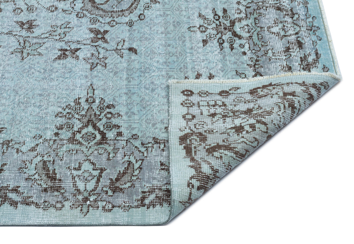 Light blue and brown distressed rug with a traditional floral medallion pattern, shown with a folded corner.