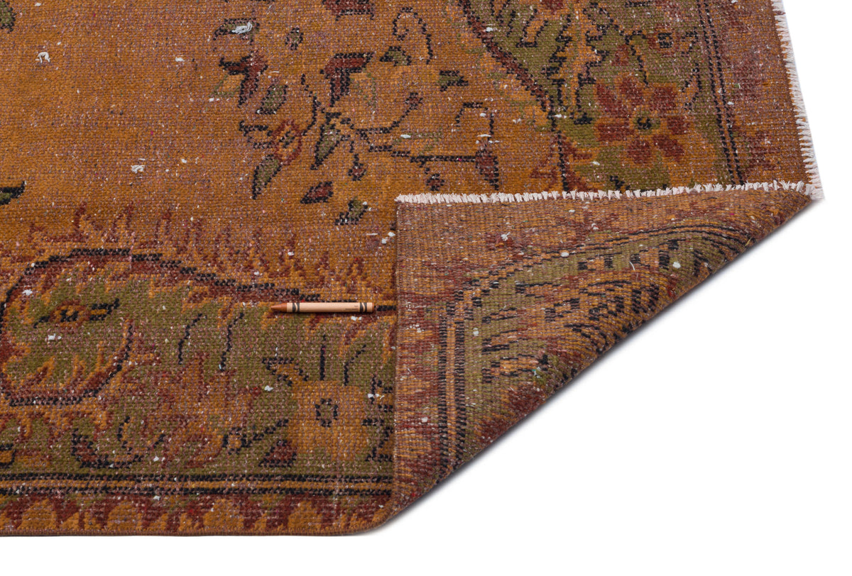 Distressed rust-orange rug with green and brown floral medallion patterns and a folded corner showing the woven backing.