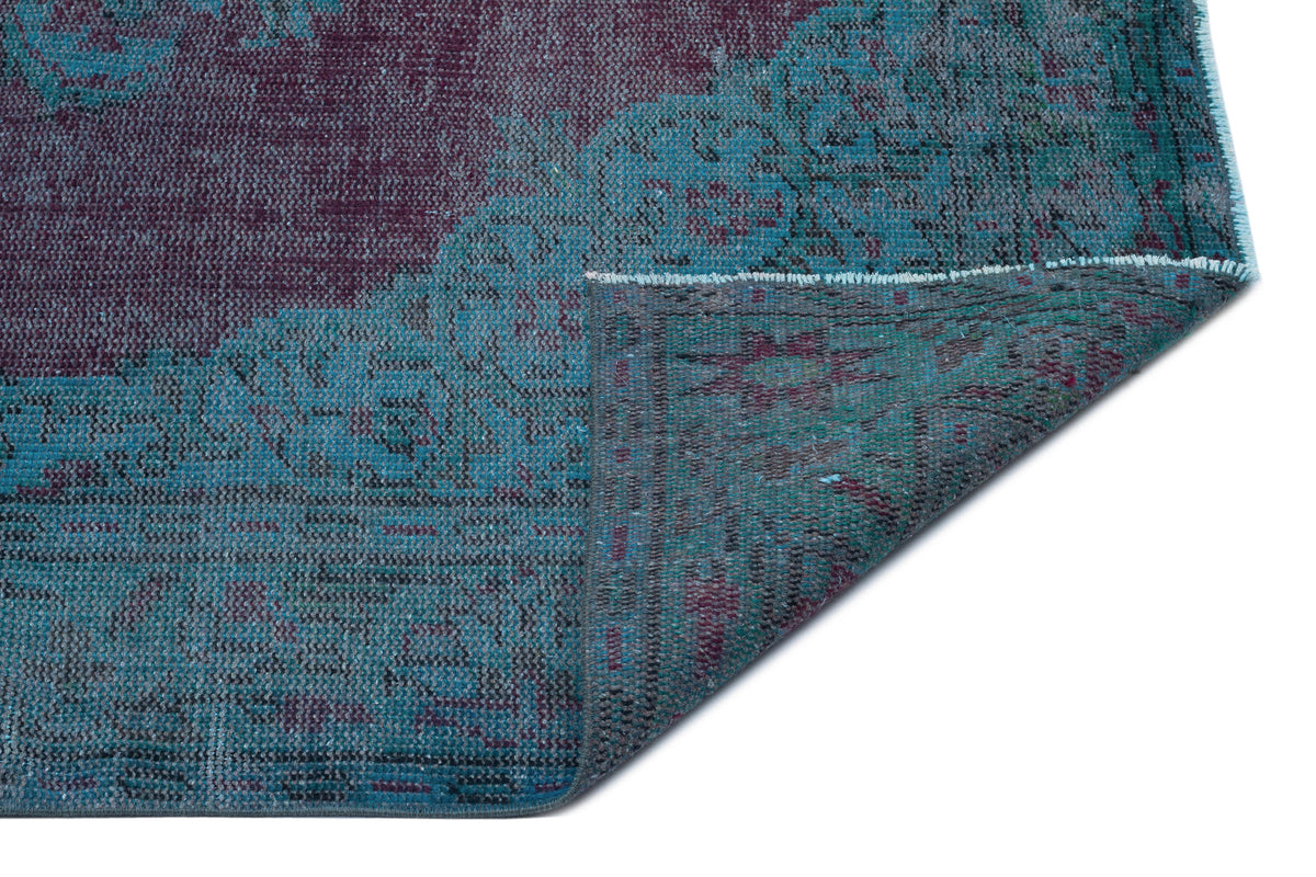 Distressed teal and plum vintage-style rug with a folded corner revealing the underside texture on a white background.