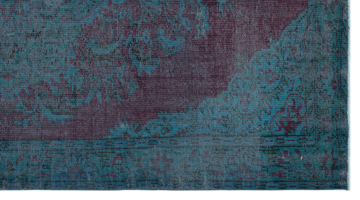 Distressed deep purple and teal rug with an ornate, faded floral medallion pattern.