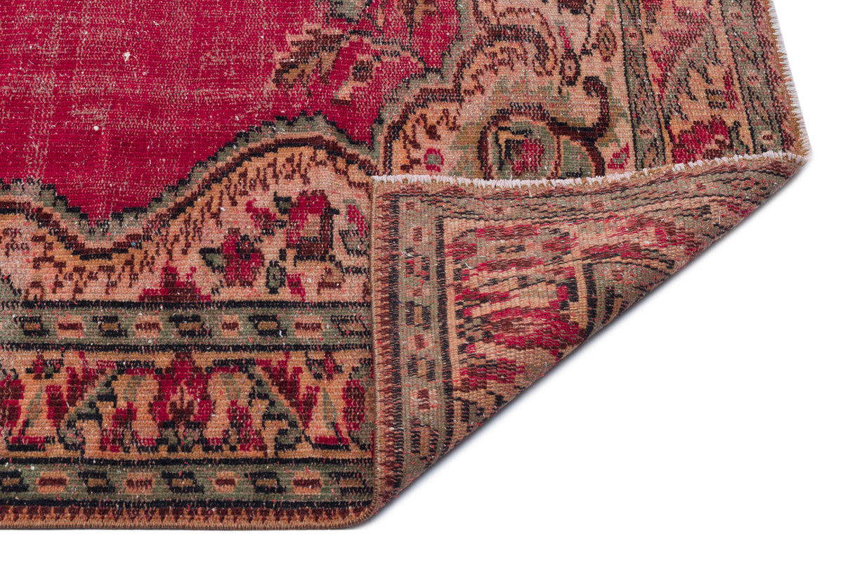 Distressed red, green, and beige vintage-style rug with a floral medallion pattern, shown with a folded corner.
