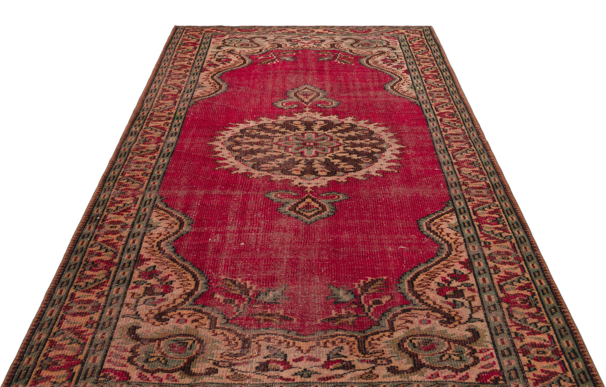 Distressed red vintage rug with a central dark medallion, ornate floral borders, and muted green and beige accents.