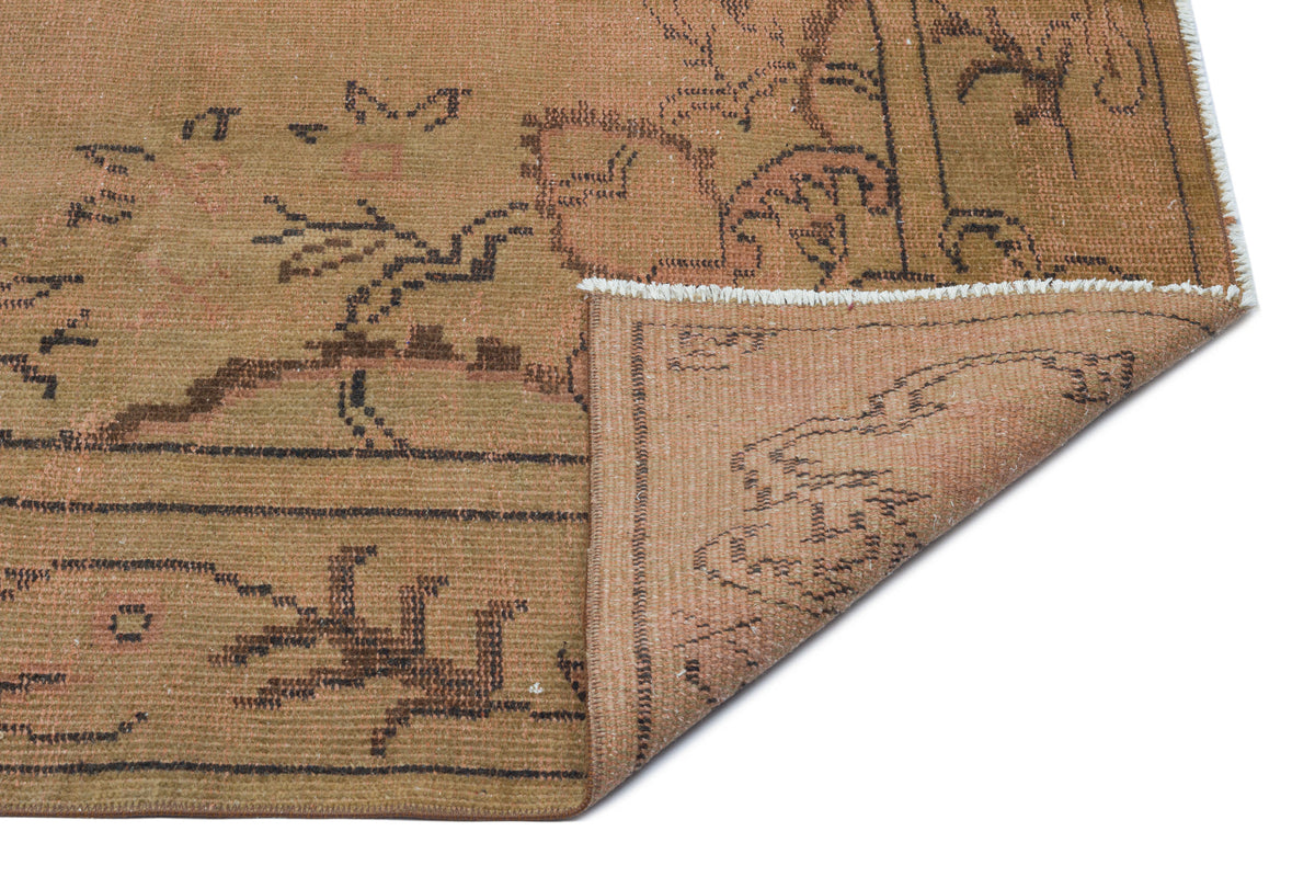 Tan and brown vintage-style rug with a faded floral pattern, shown with a corner folded over on a white background.