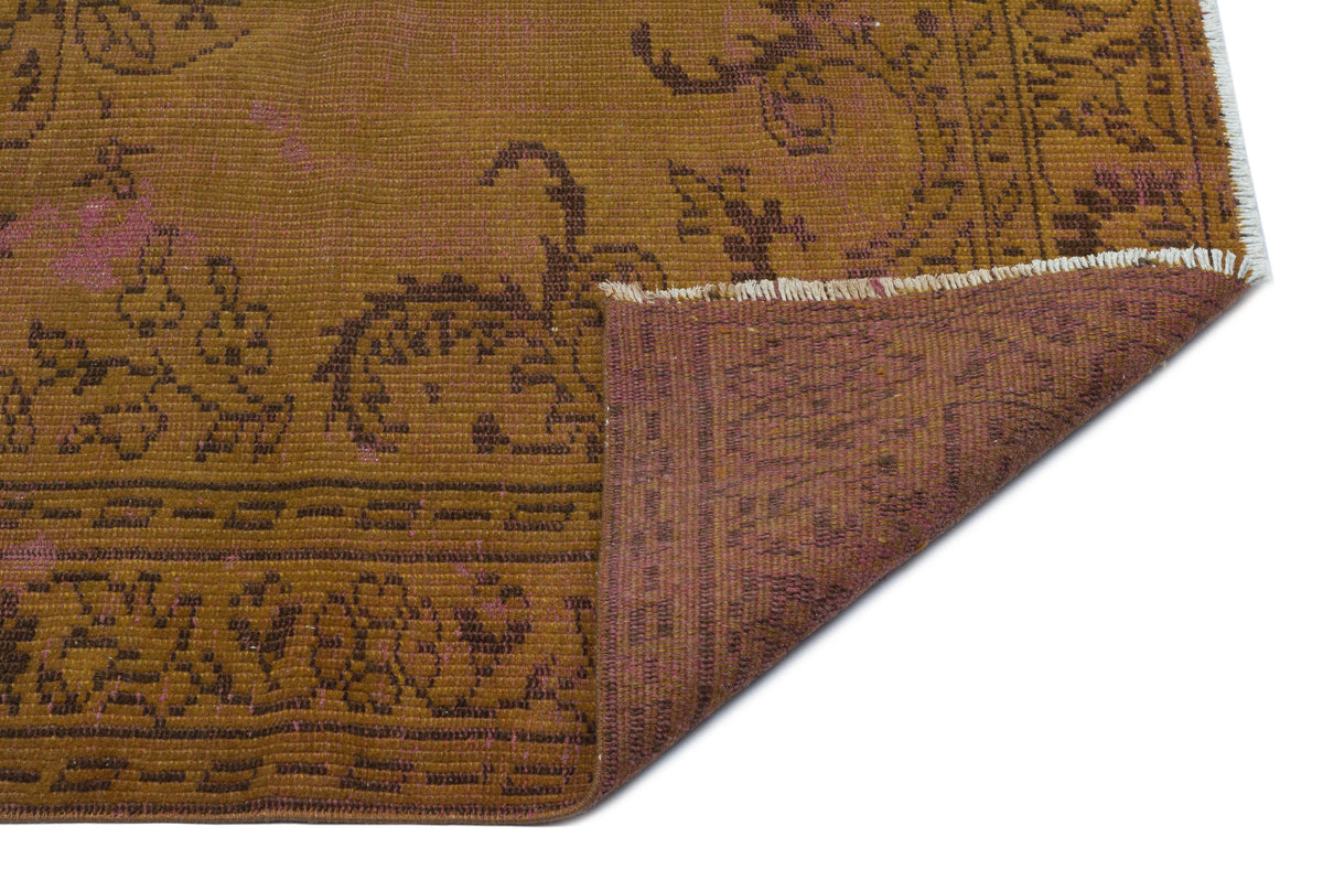 Mustard yellow and brown distressed rug with a floral medallion pattern, showing a folded corner with a purple underside.