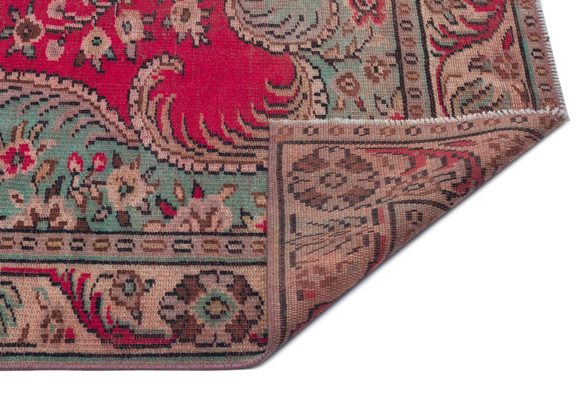Red, sage green, and beige traditional rug with a floral medallion pattern, shown with a corner folded over.