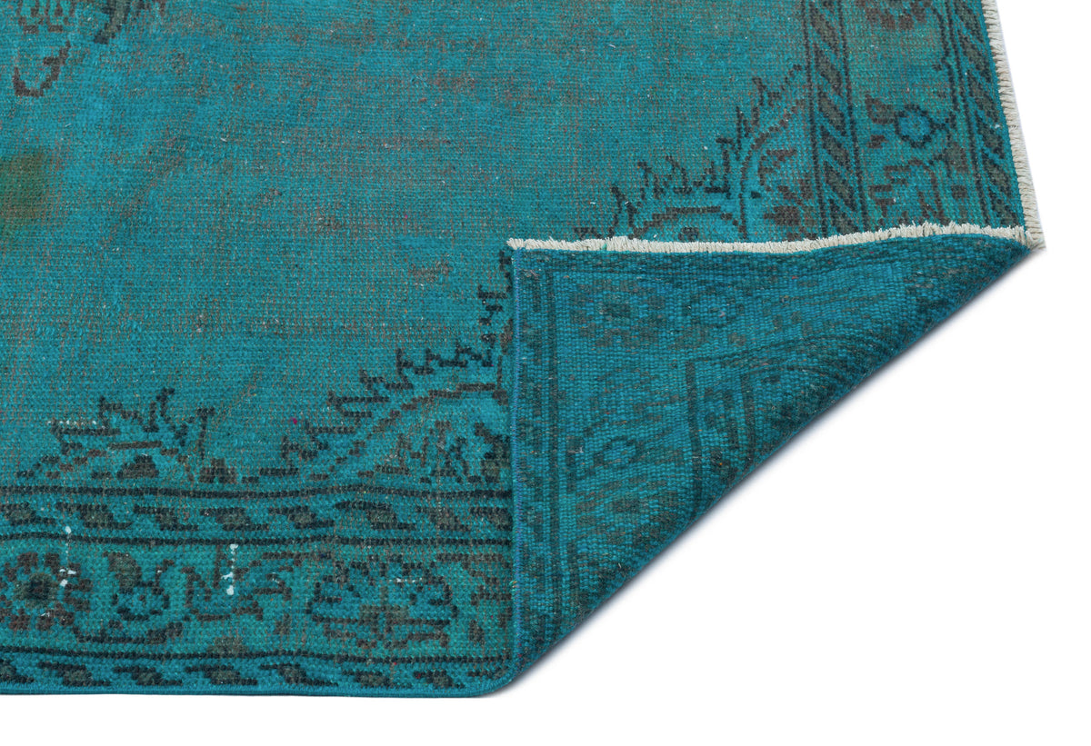 Teal vintage-style rug with a dark grey floral border and a folded corner showing the underside weave.