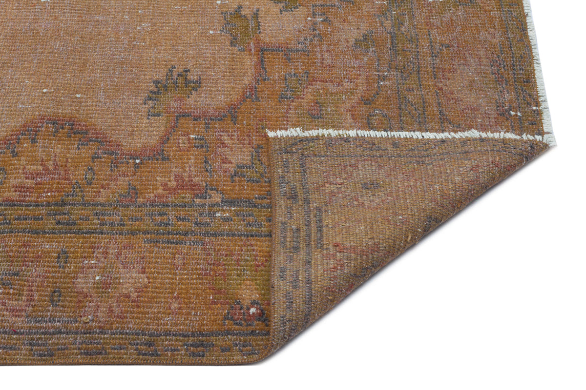 Distressed rust and brown vintage-style rug with a faded floral medallion pattern and a folded corner.