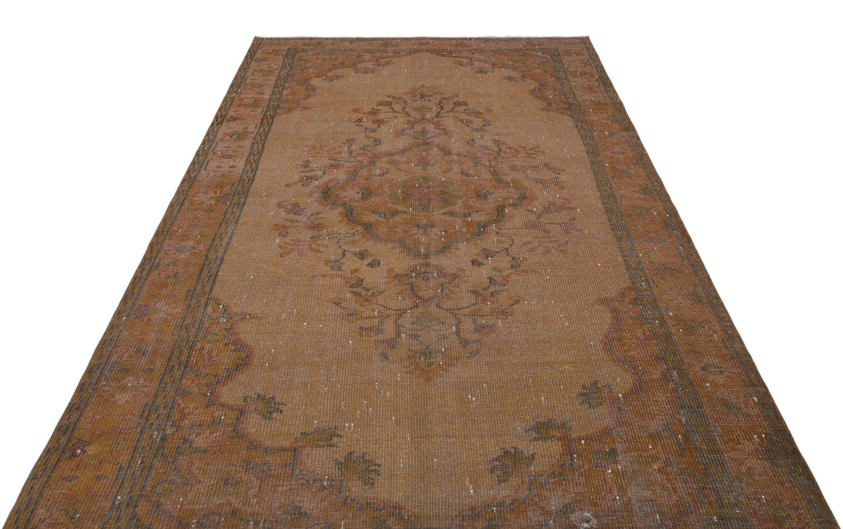 Distressed rust-colored vintage rug with a central floral medallion and ornate border on a white background.