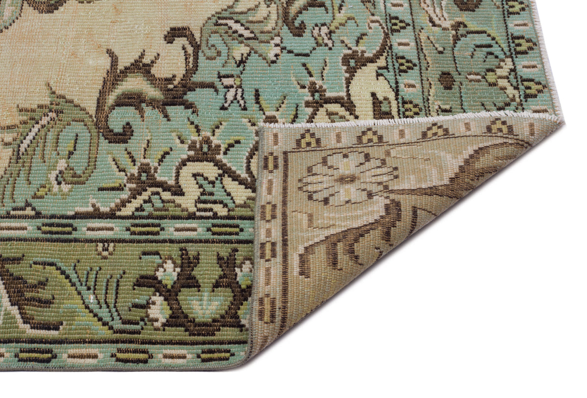 Distressed sage green and beige rug with a traditional floral medallion pattern, shown with a corner folded over.