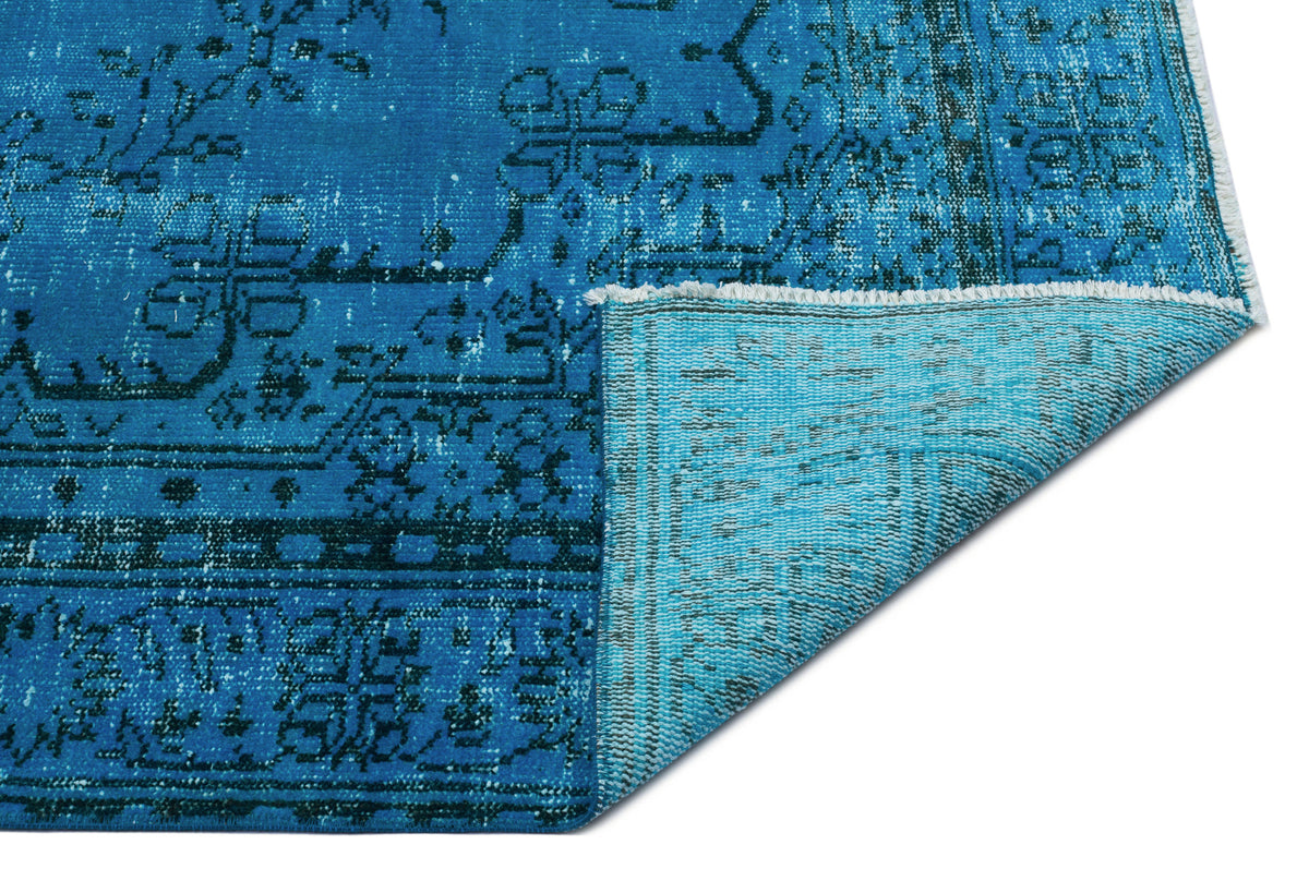 Bright blue distressed rug with a dark geometric medallion pattern and a folded corner showing the lighter blue backing.