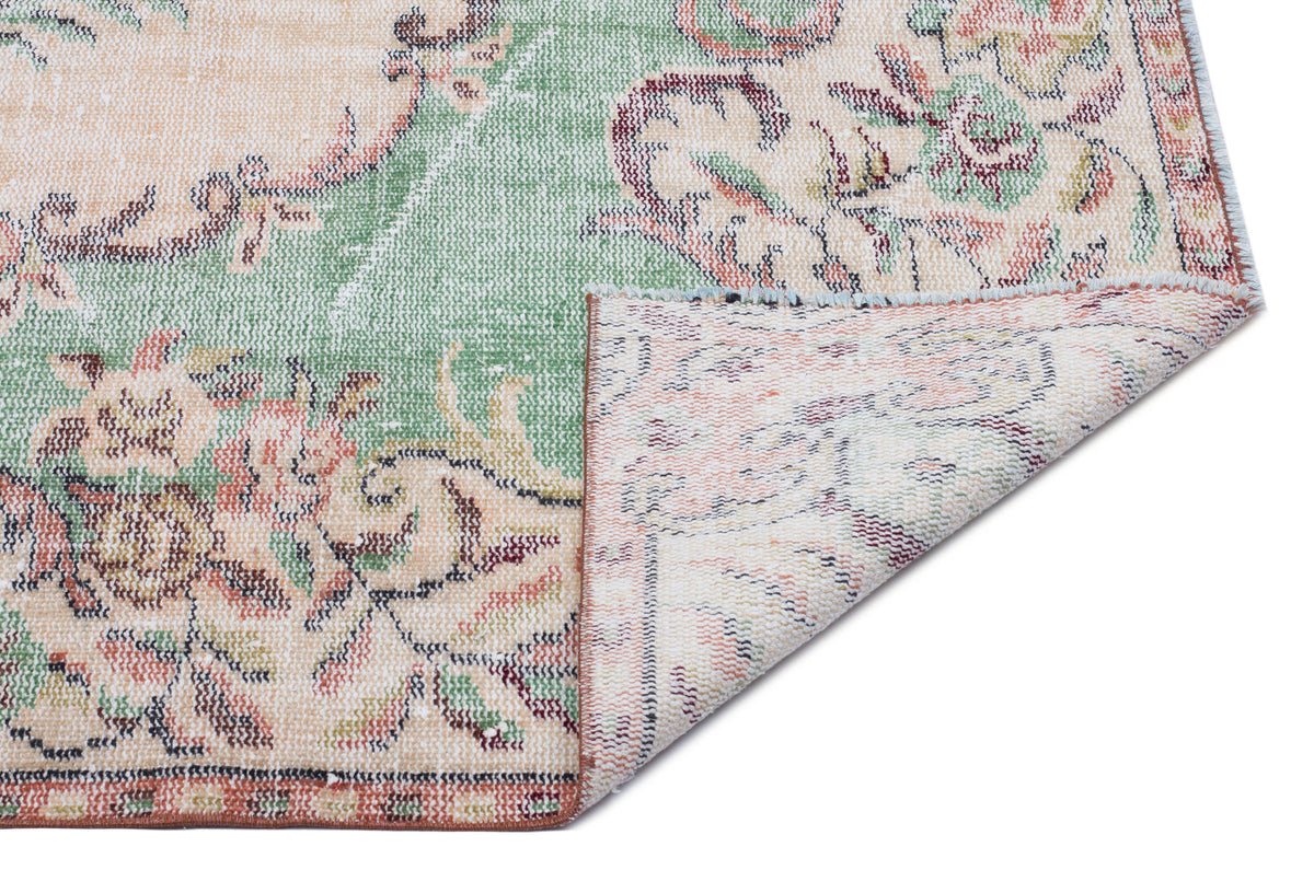 Distressed floral rug in sage green, peach, and cream with a folded corner revealing the woven backing.