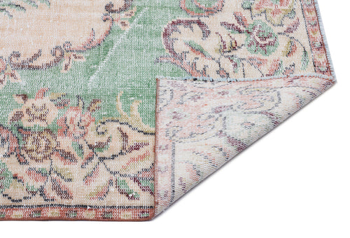 Load image 1 in gallery view. Distressed floral rug in sage green, peach, and cream with a folded corner revealing the woven backing.