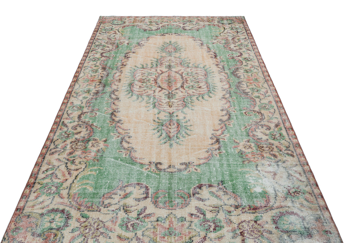 Distressed vintage-style rug with a green and peach floral medallion pattern on a white background.