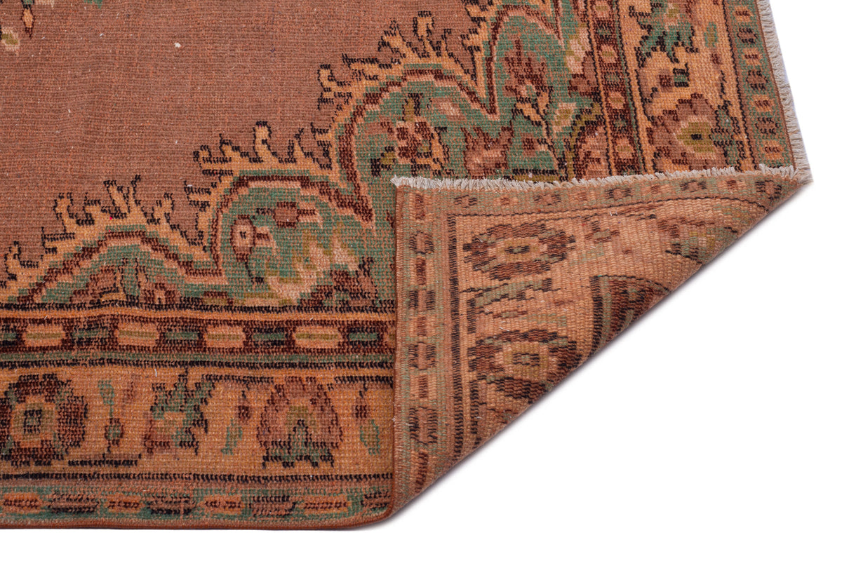 Rust and green traditional rug with a floral medallion pattern and a folded corner showing the underside.