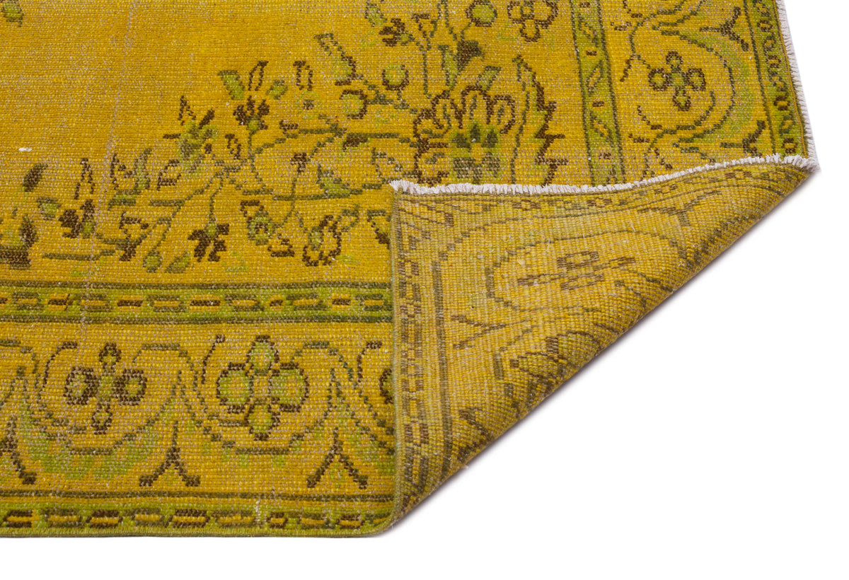 Mustard yellow and olive green vintage-style rug with a floral border and corner fold, isolated on a white background.