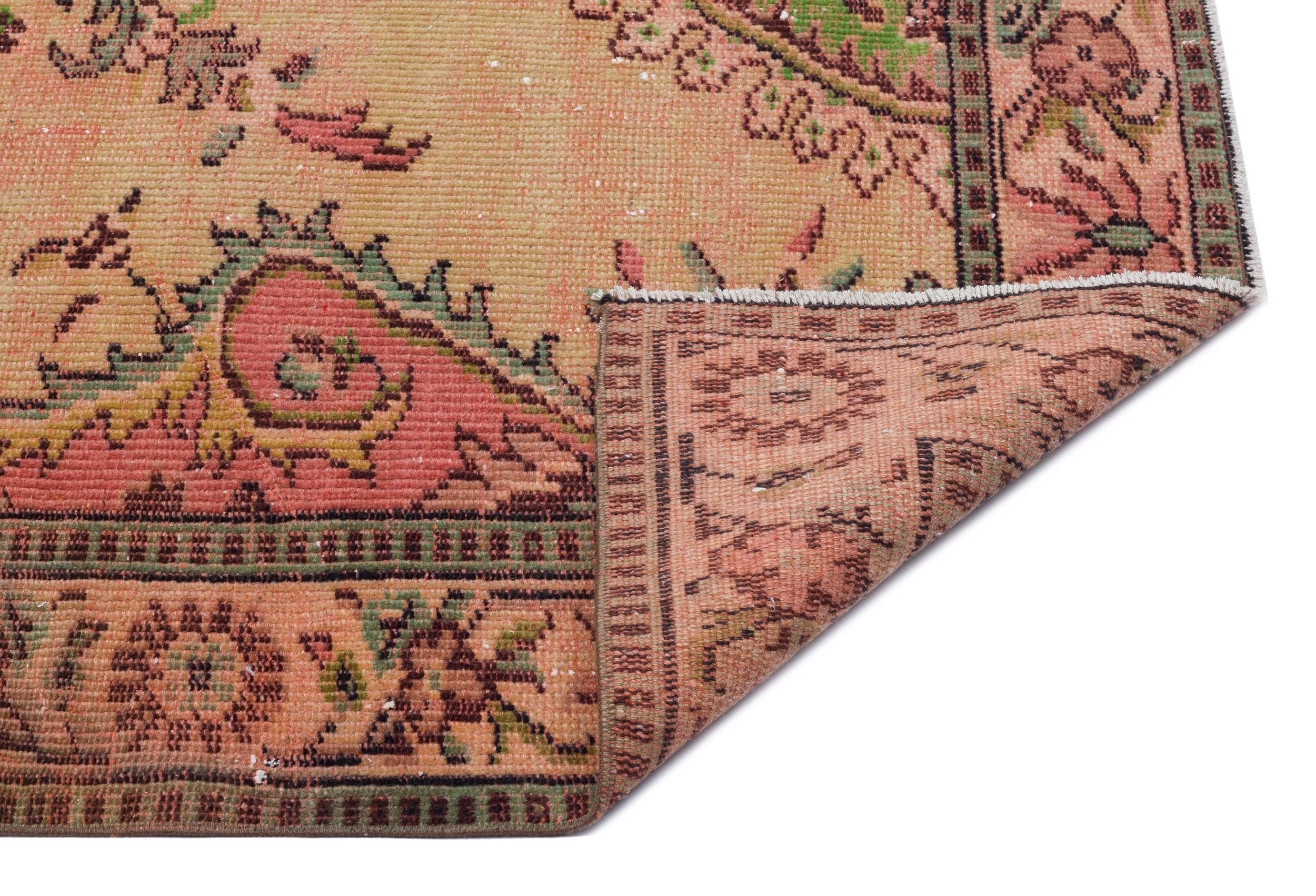 Distressed peach, green, and tan vintage-style rug with a floral medallion pattern, shown with a corner folded over.
