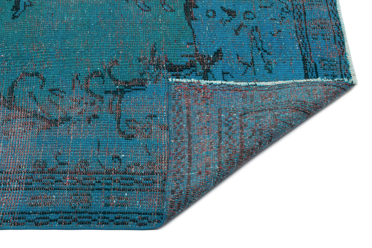 Teal and black distressed vintage-style rug with a folded corner revealing the woven backing.