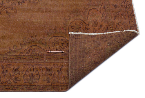 Load image 1 in gallery view. Rust-colored vintage rug with a faded floral pattern and white fringe, shown with a corner folded over.