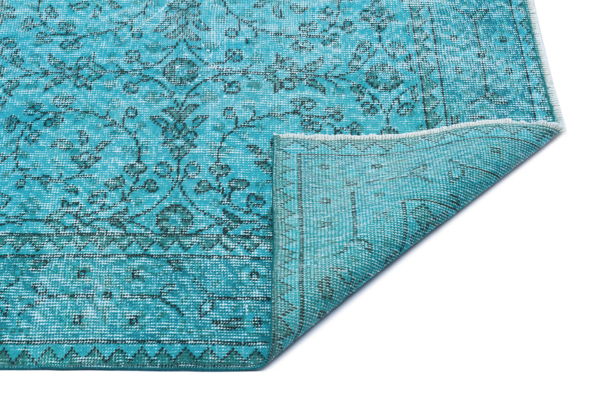 Turquoise rug with a dark grey floral pattern and a folded corner revealing the woven backing.