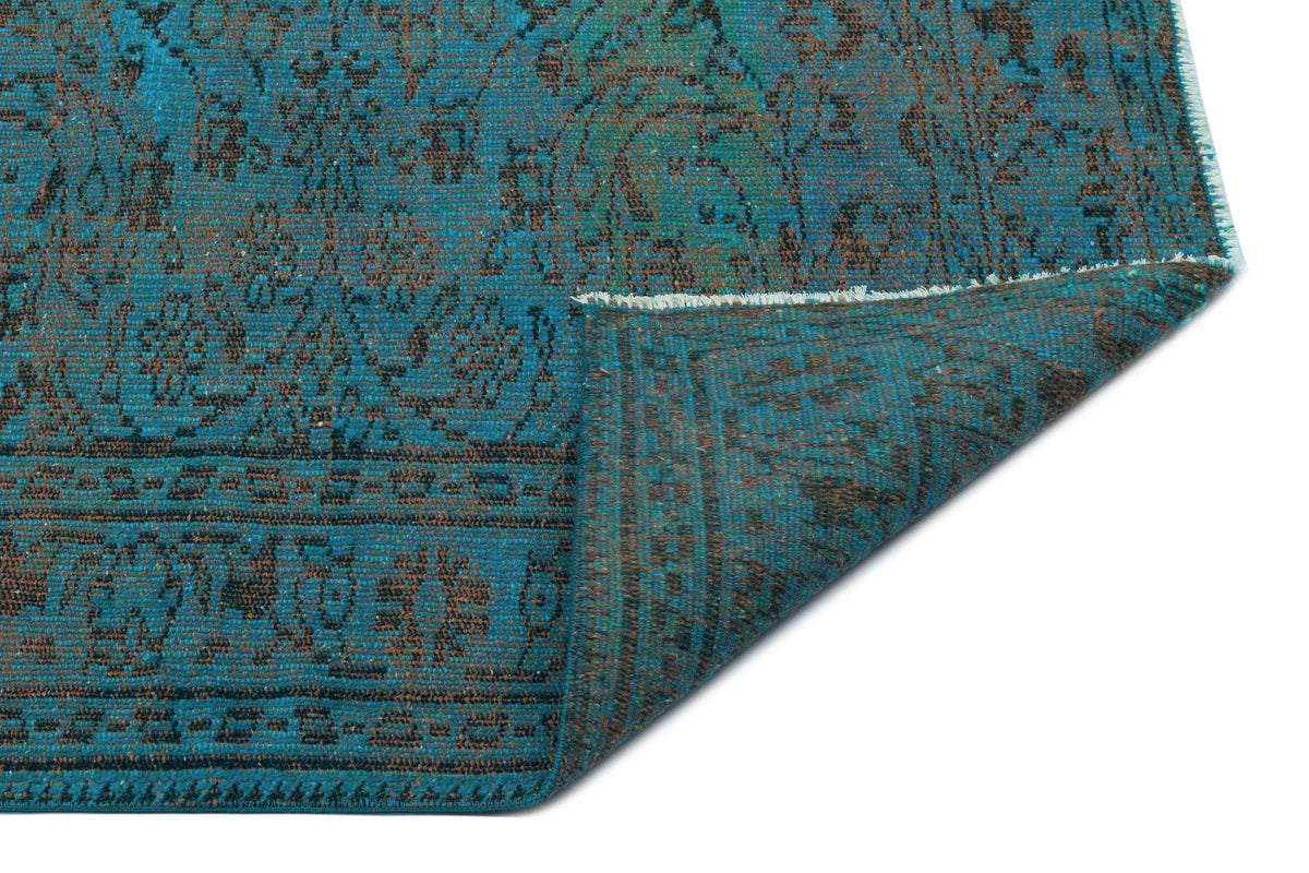 Teal and brown distressed traditional rug with an ornate floral pattern, shown with a corner folded over.