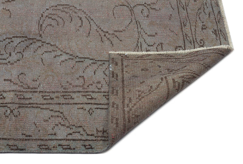 Load image 1 in gallery view. Taupe and brown distressed rug with a faded floral pattern and a folded corner showing the woven backing.