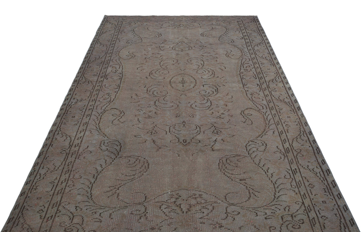 Faded taupe and brown vintage rug with a central floral medallion and ornate border on a white background.