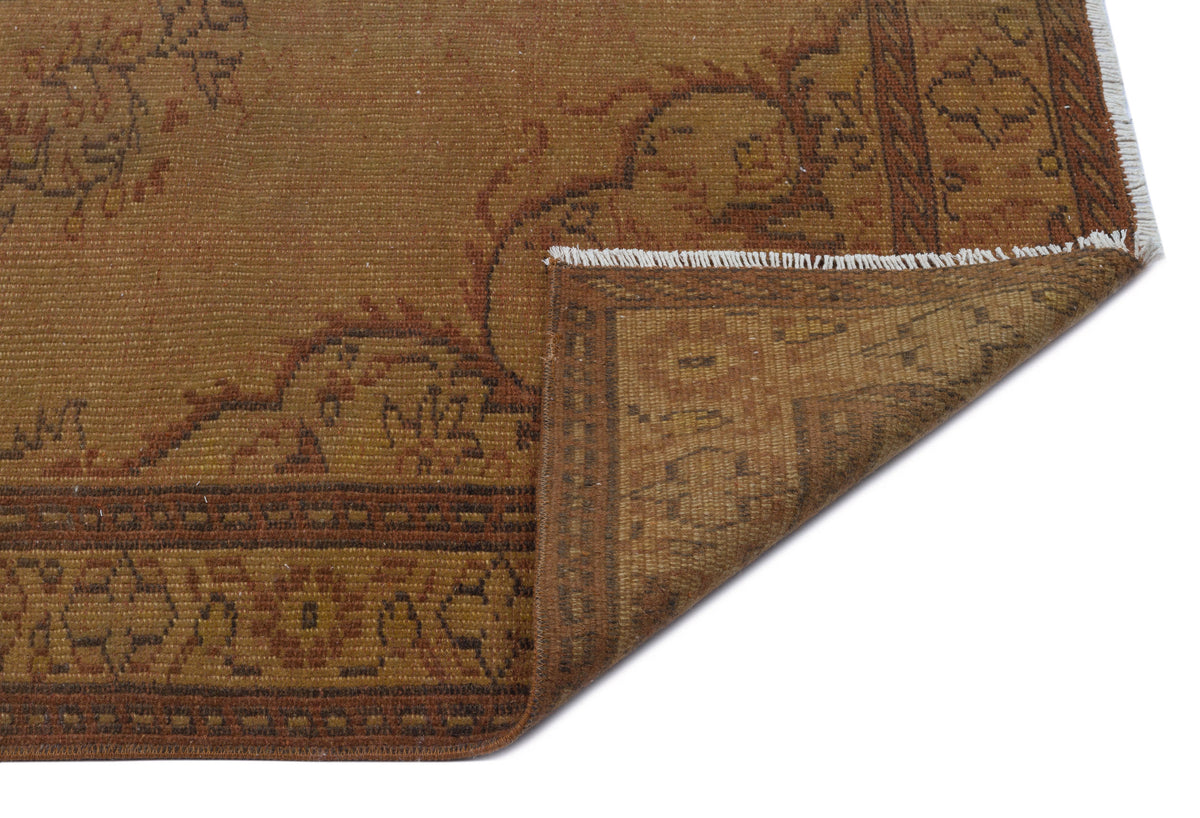 Brown and rust-colored vintage rug with a traditional floral border and a folded corner showing white fringe.